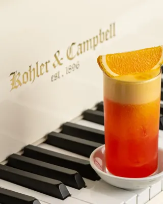 Orange-topped girabaldi cocktail placed on the keys of a white Kohler and Campbell piano.