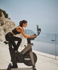 Guest cycling on an outdoor exercise bike overlooking coastal cliffs and the sea.