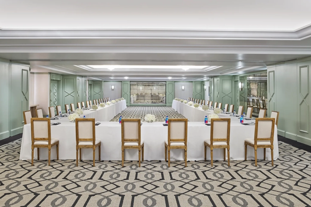 The Gallery set in U-shape for a meeting: white-linen tables, wood chairs, hydrangea centerpieces, and pads with pens.