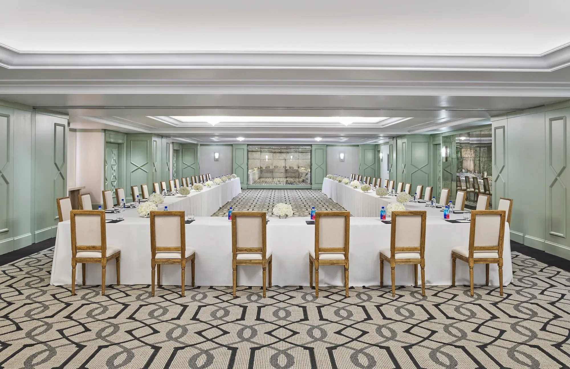The Gallery set in U-shape for a meeting: white-linen tables, wood chairs, hydrangea centerpieces, and pads with pens.