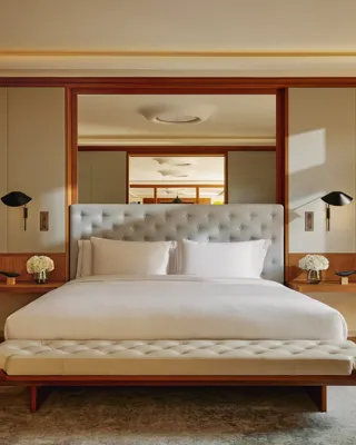 Bedroom in The Apartment featuring a king bed with a tall tufted headboard, flanked by black wall lights, with neutral tones and wood accents.