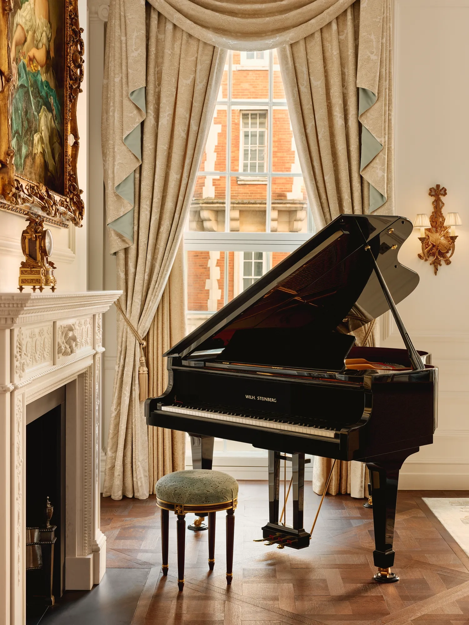 Elegant room with a black grand piano beside an ornate white fireplace, framed by tall draped curtains and a window overlooking red brick architecture.