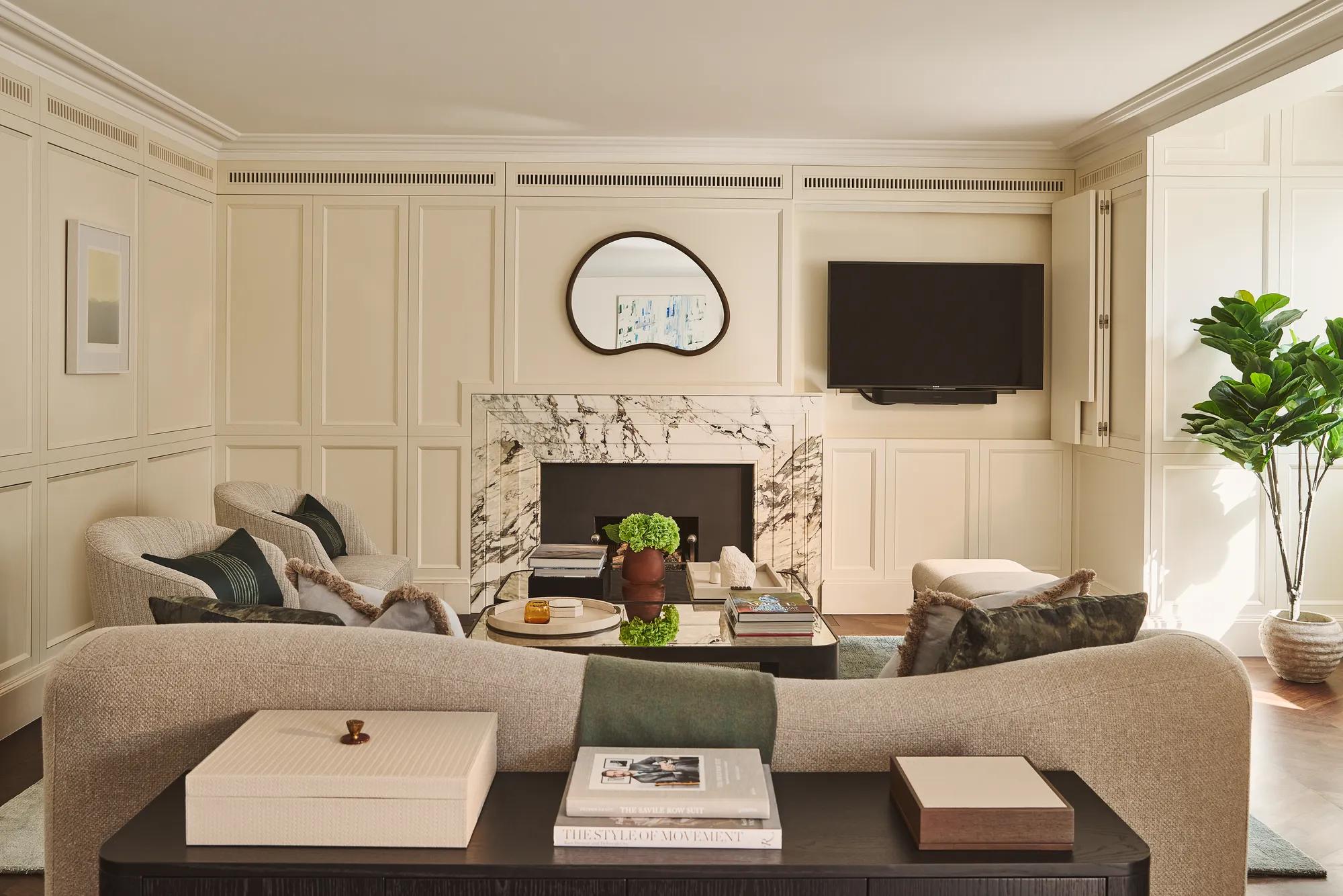 Bright living room with marble fireplace, curved sofa, armchairs, wall-mounted TV, and coffee table.