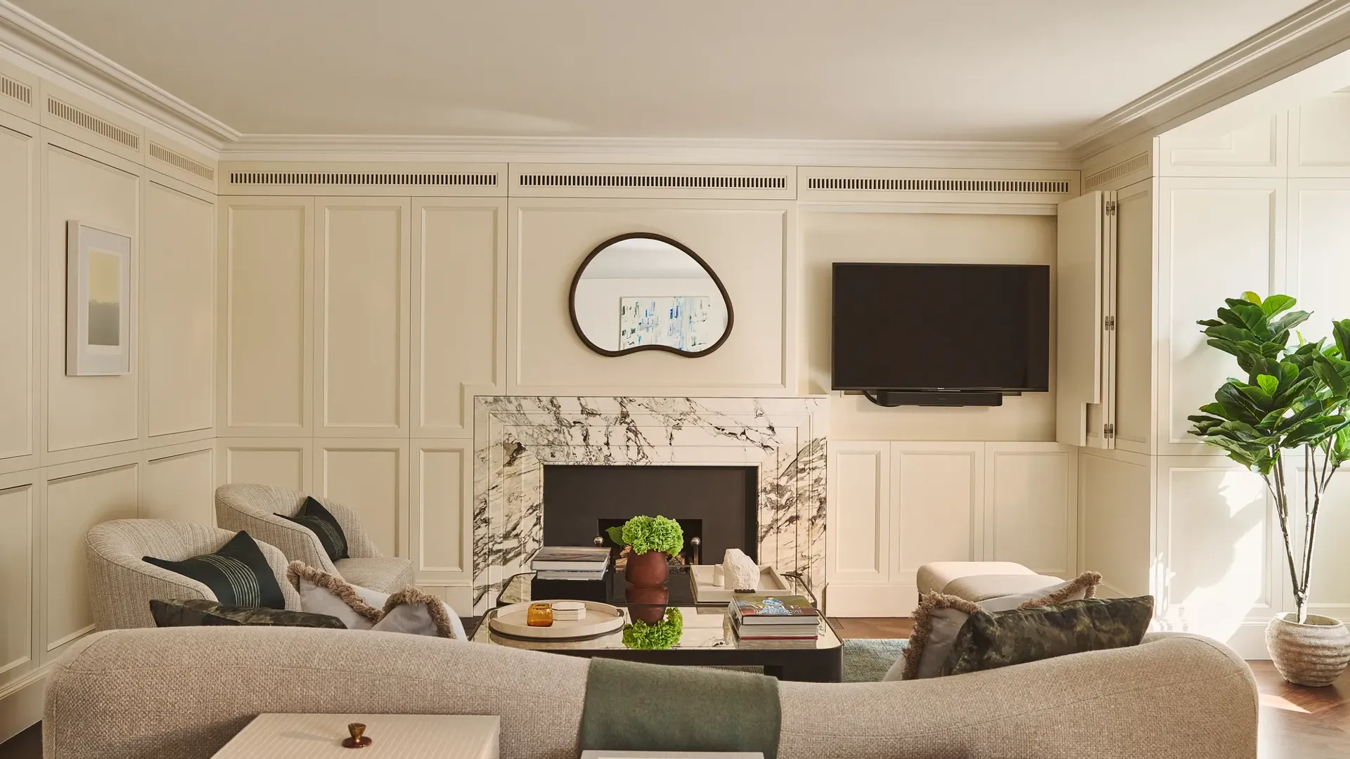 Bright living room with marble fireplace, curved sofa, armchairs, wall-mounted TV, and coffee table.
