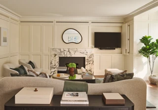 Bright living room with marble fireplace, curved sofa, armchairs, wall-mounted TV, and coffee table.