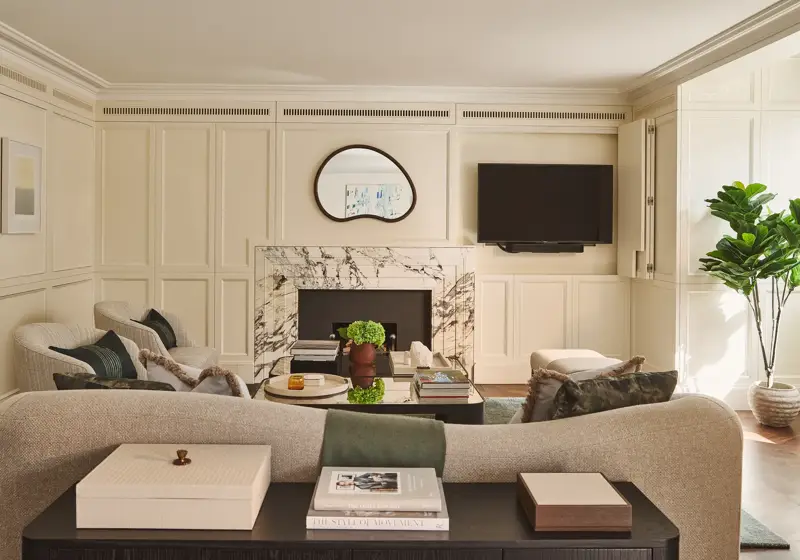 Bright living room with marble fireplace, curved sofa, armchairs, wall-mounted TV, and coffee table.