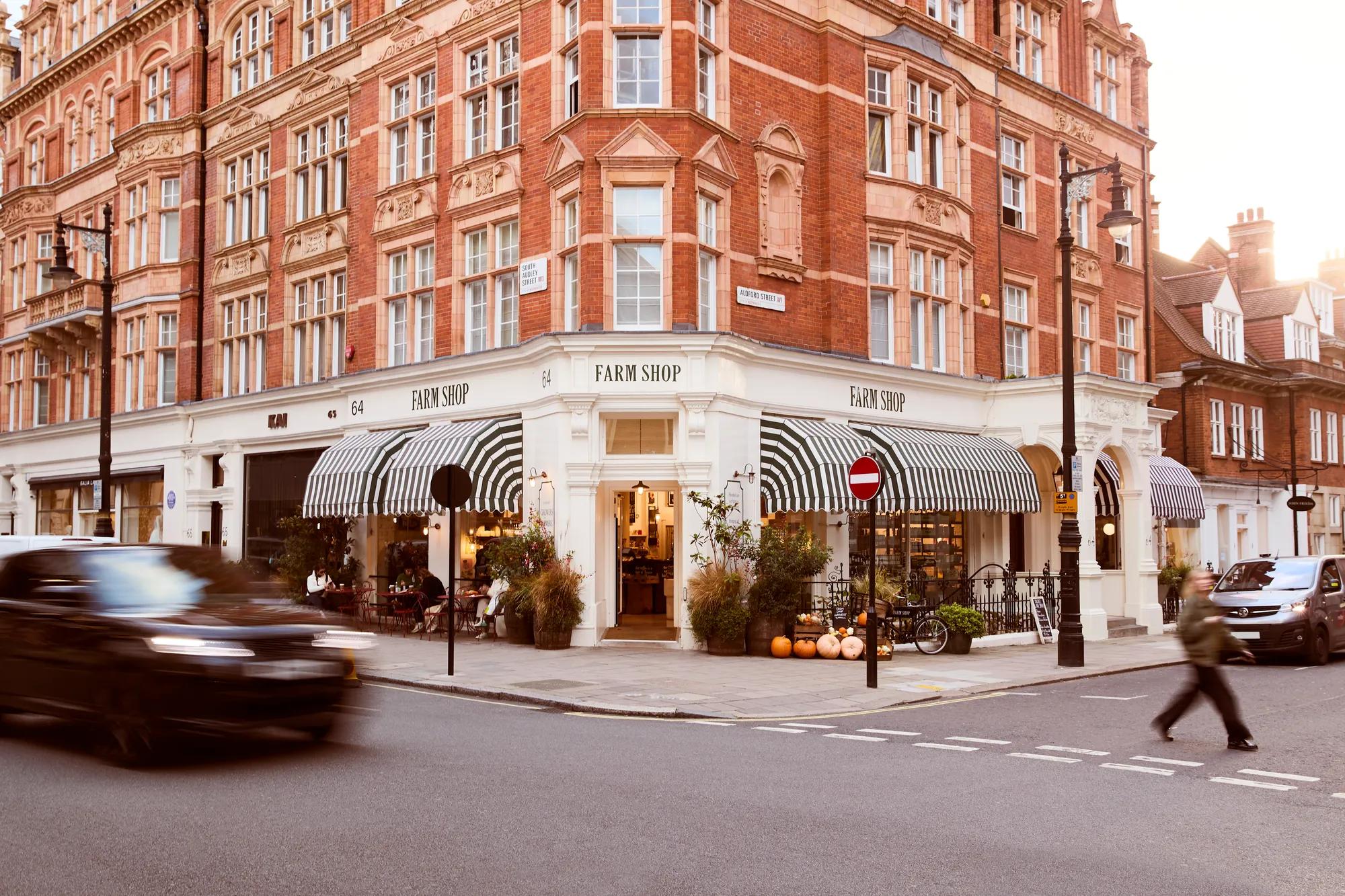 Corner Farm Shop with striped awnings in a red-brick building, as traffic and pedestrians pass by.