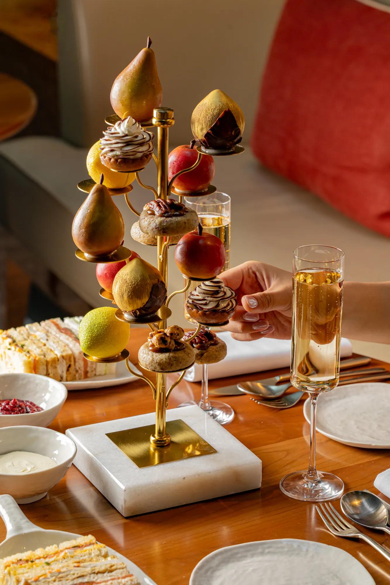 Fruit-inspired afternoon tea stand with pastries and fresh fruit, served alongside sparkling wine and finger sandwiches.