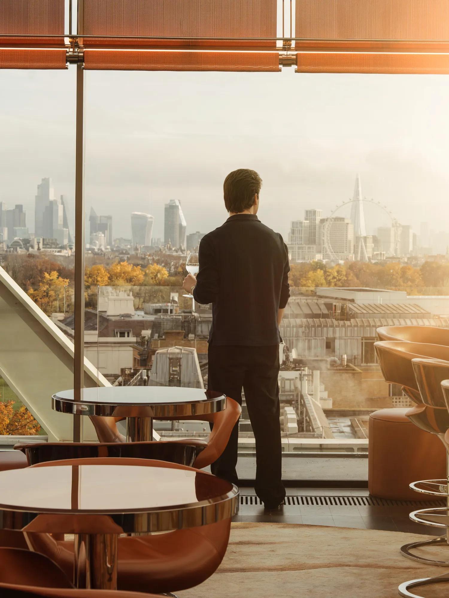 A man standing facing a view of London city with seating in the foreground