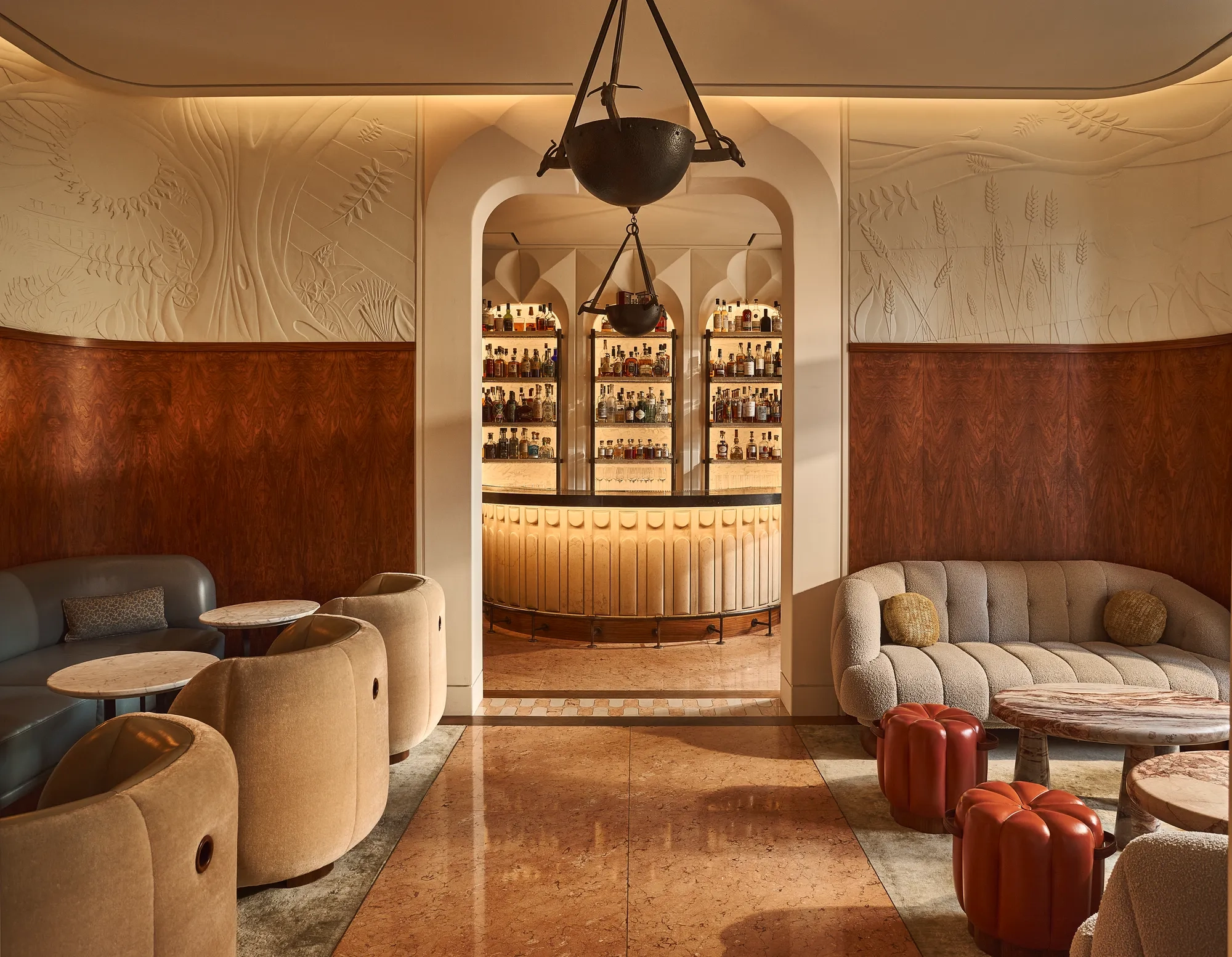 Elegant lounge with curved seating and marble tables, opening onto a softly lit bar framed by an arched doorway.