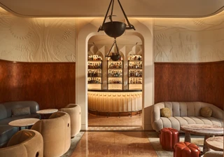 Elegant lounge with curved seating and marble tables, opening onto a softly lit bar framed by an arched doorway.