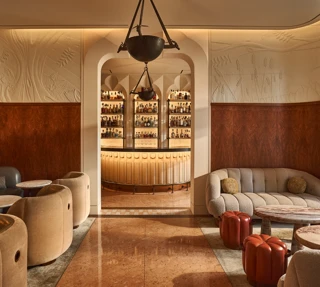 Elegant lounge with curved seating and marble tables, opening onto a softly lit bar framed by an arched doorway.