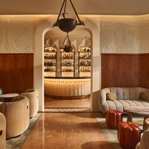 Elegant lounge with curved seating and marble tables, opening onto a softly lit bar framed by an arched doorway.