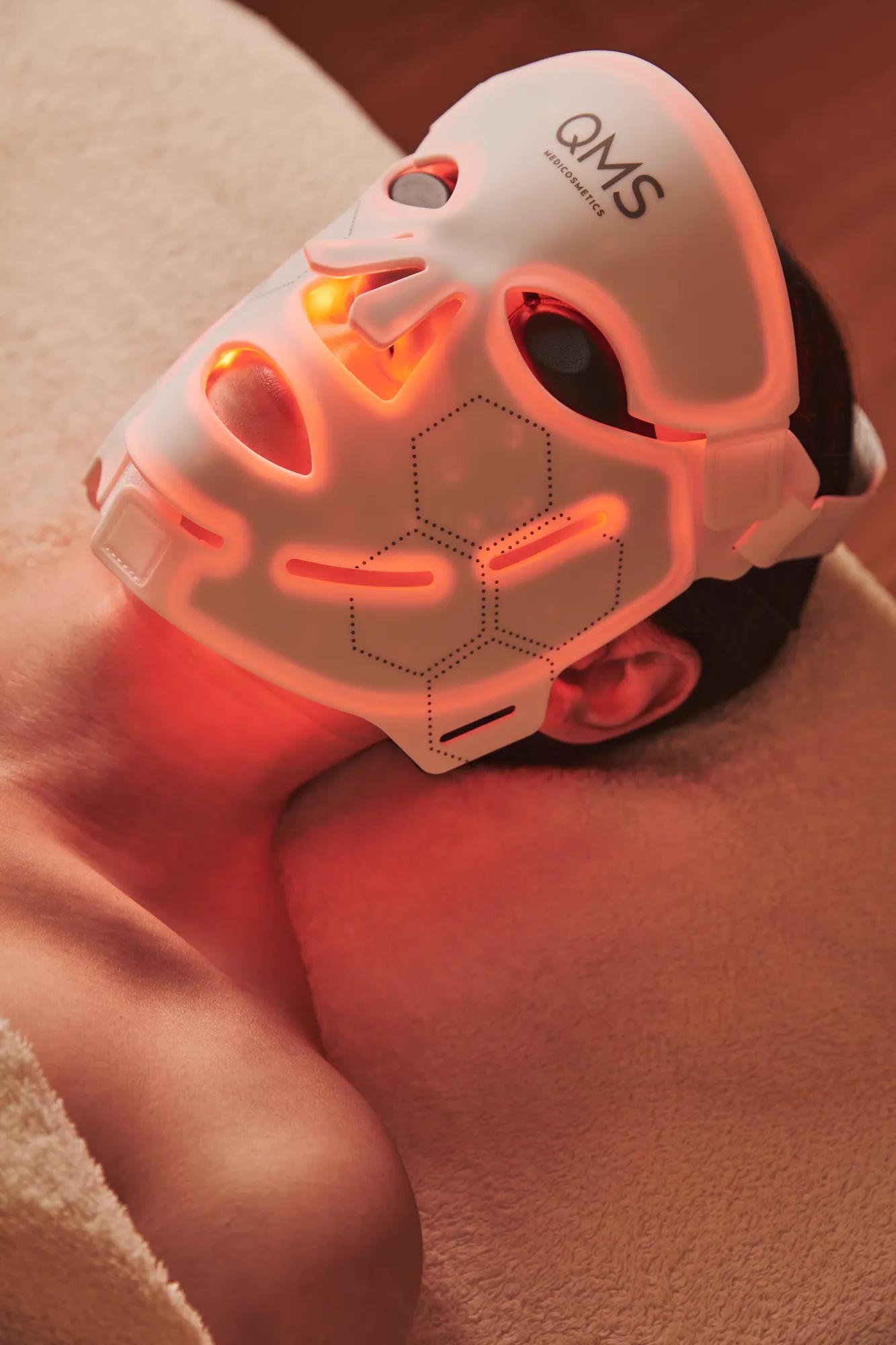 Guest lying on spa bed wearing illuminated LED facial mask during skincare treatment.