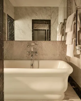 Elegant marble bathroom with a freestanding white bathtub, wall-mounted taps, and plush towels neatly hung on a chrome rail under soft ambient lighting.