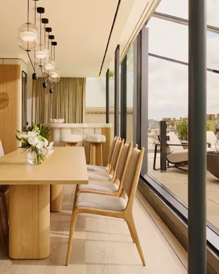 ChatGPT said:

A bright dining area with a wooden table and chairs, pendant lighting, and glass doors opening to a terrace with city views