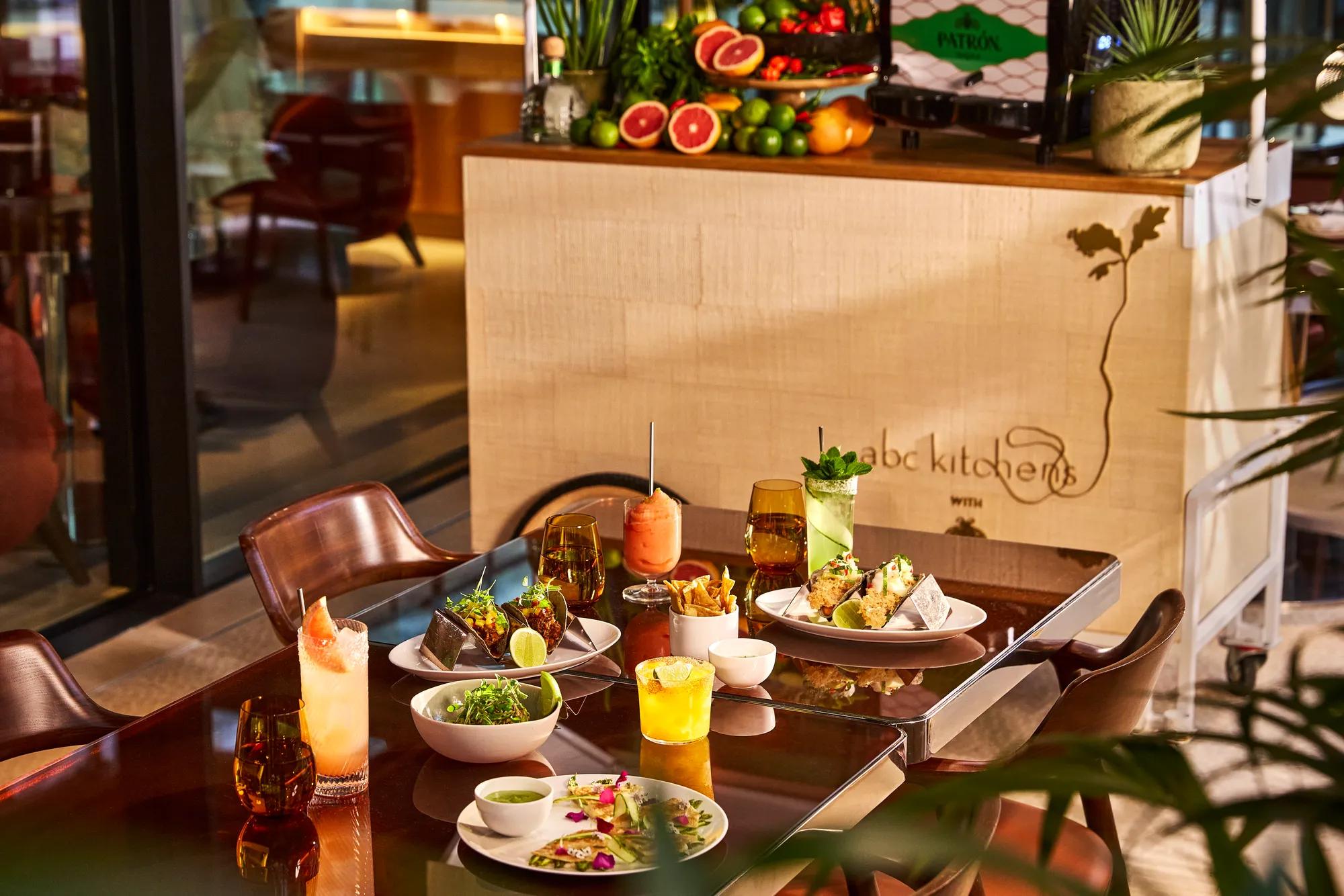 Dining table at abc kitchens with tacos, cocktails, fries and shared plates in warm evening light.