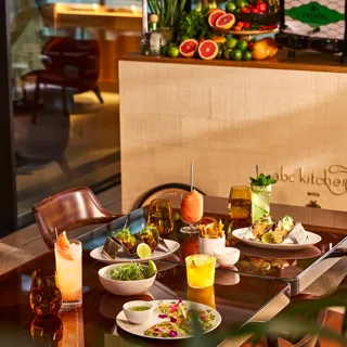 Dining table at abc kitchens with tacos, cocktails, fries and shared plates in warm evening light.