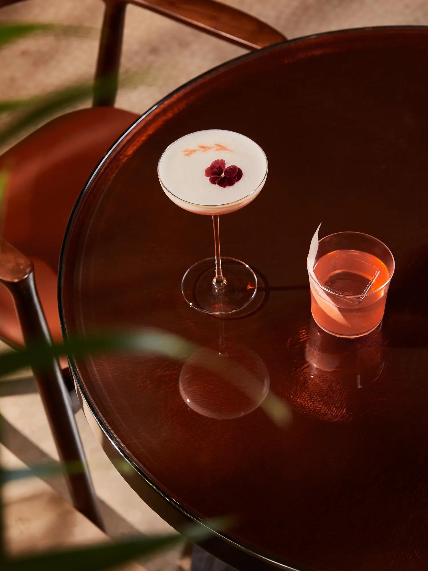 A wooden table with two colorful cocktails placed side by side.