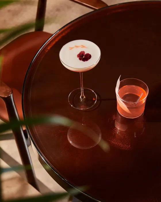 A wooden table with two colorful cocktails placed side by side.