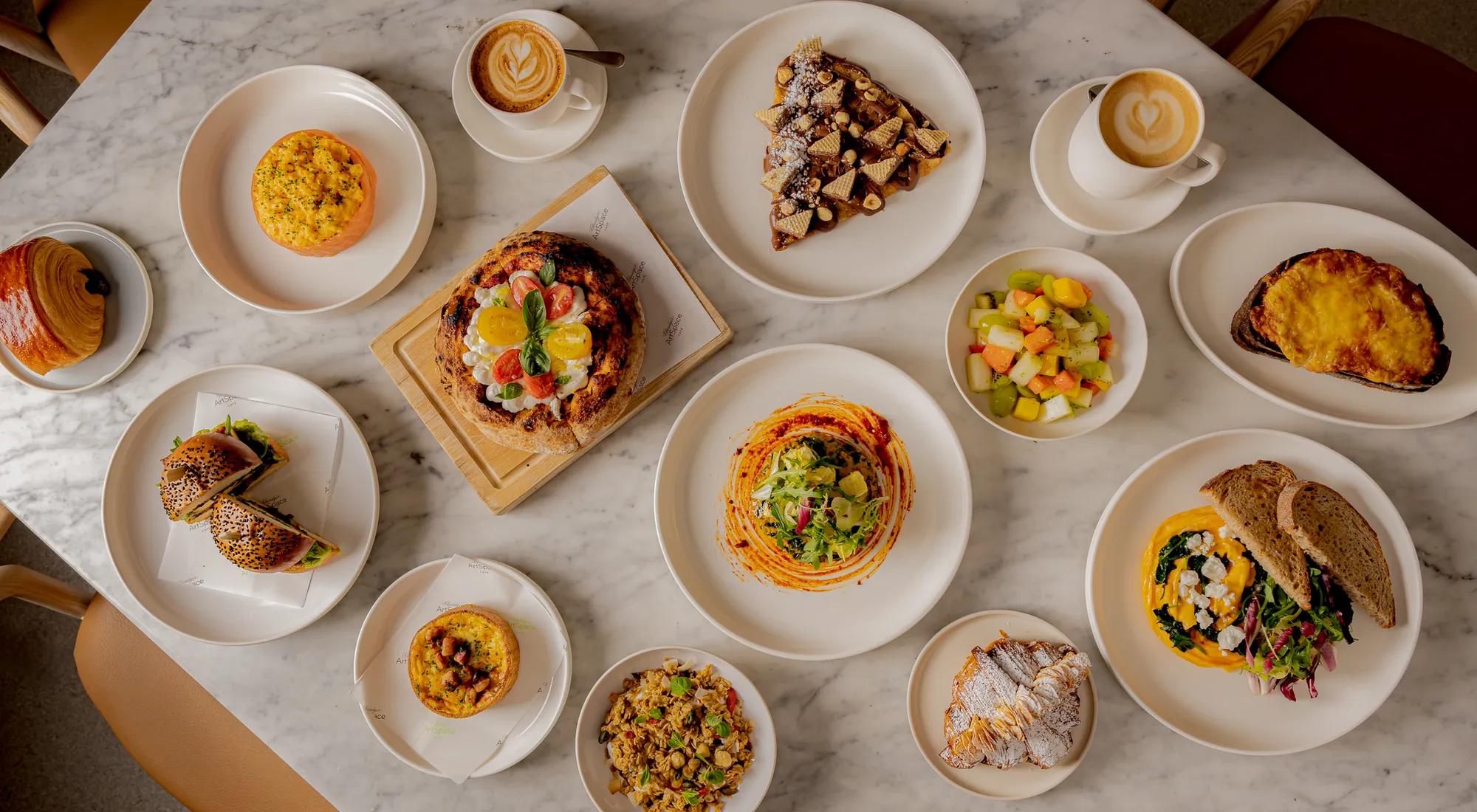 **Alt text (WCAG 2.2 AA):**
Overhead view of a marble table set with brunch dishes including pizzas, pastries, salads, sandwiches, coffee and fresh fruit.

