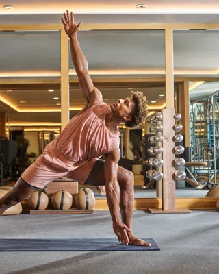 Person practicing a yoga pose on a mat in a modern fitness studio with mirrors and gym equipment.