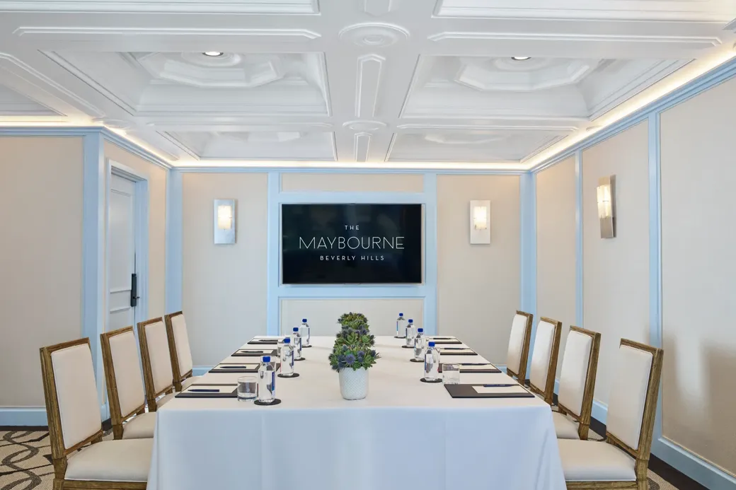 Wilshire Room boardroom setup with U-shaped table, neutral chairs, water and notepads, and a wall display screen