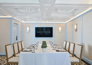 Wilshire Room boardroom setup with U-shaped table, neutral chairs, water and notepads, and a wall display screen