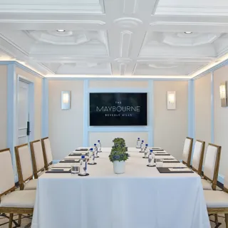 Wilshire Room boardroom setup with U-shaped table, neutral chairs, water and notepads, and a wall display screen