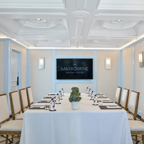 Wilshire Room boardroom setup with U-shaped table, neutral chairs, water and notepads, and a wall display screen