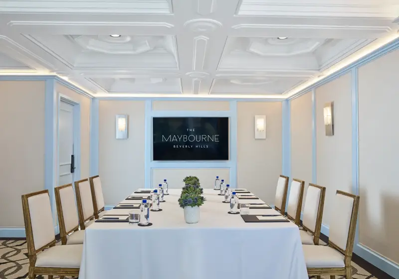 Wilshire Room boardroom setup with U-shaped table, neutral chairs, water and notepads, and a wall display screen