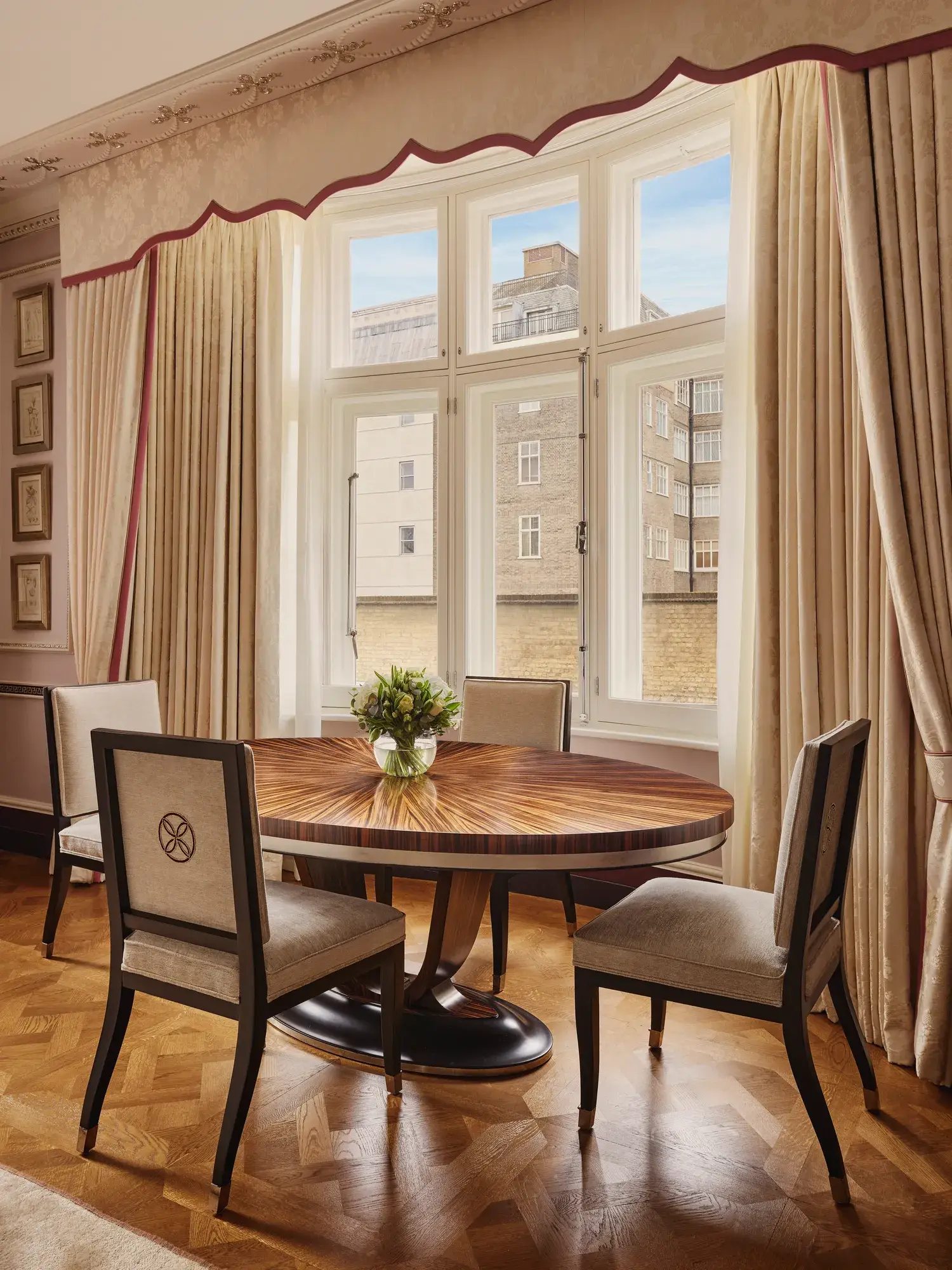 Elegant dining nook with round wooden table, four chairs, and large draped window.