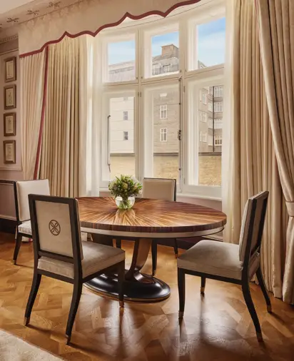 Elegant dining nook with round wooden table, four chairs, and large draped window.