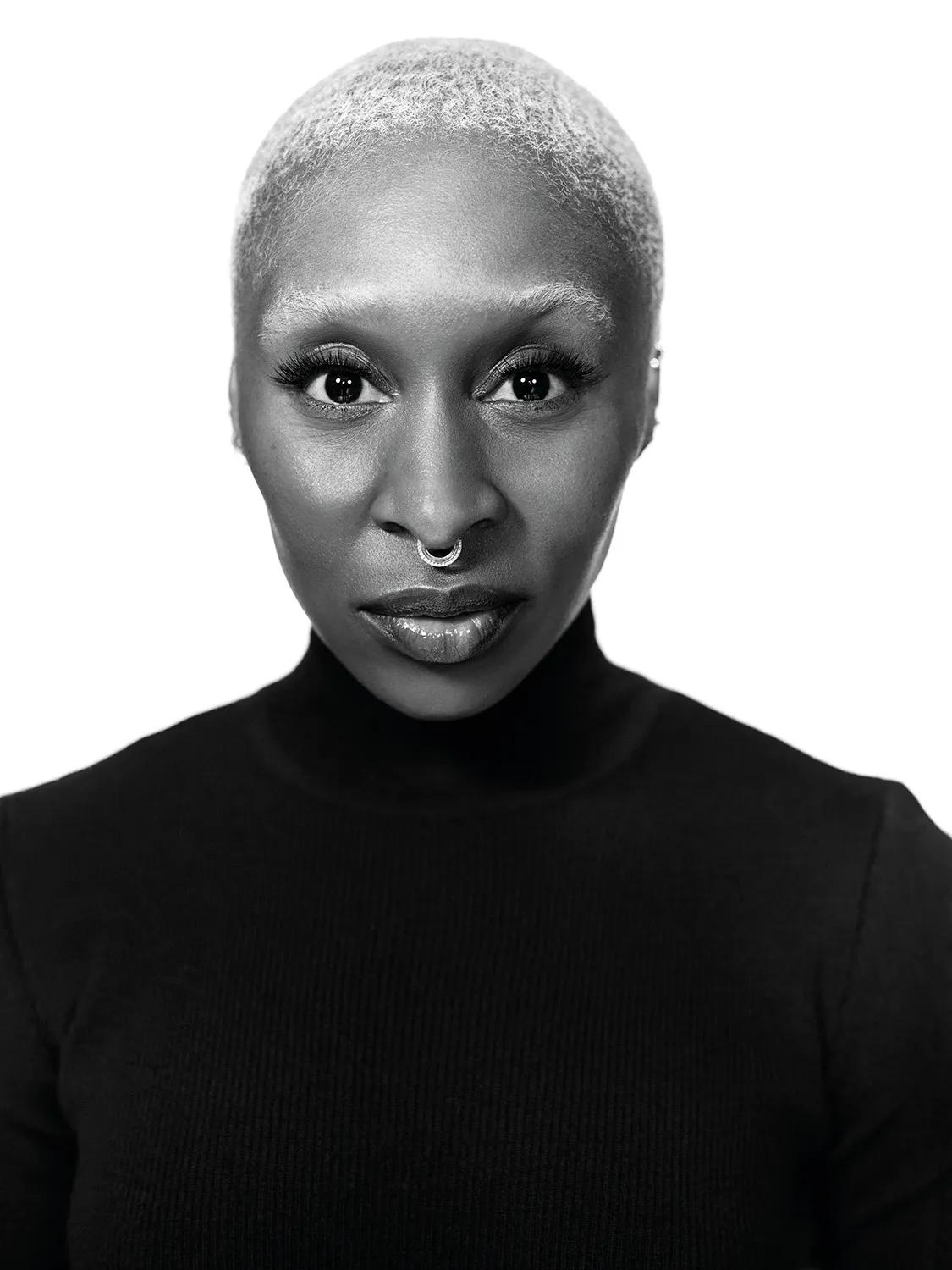 Black-and-white portrait of woman with short hair, nose ring, and intense gaze against plain background.