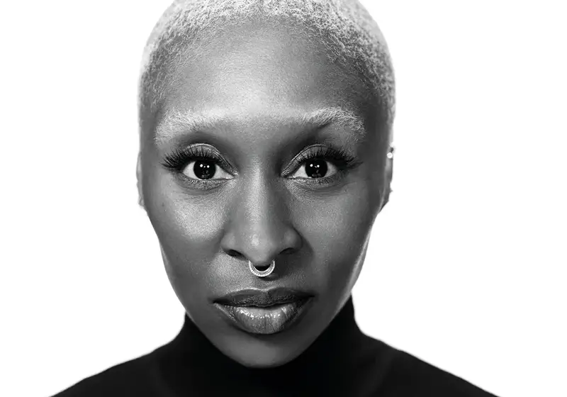 Black-and-white portrait of woman with short hair, nose ring, and intense gaze against plain background.