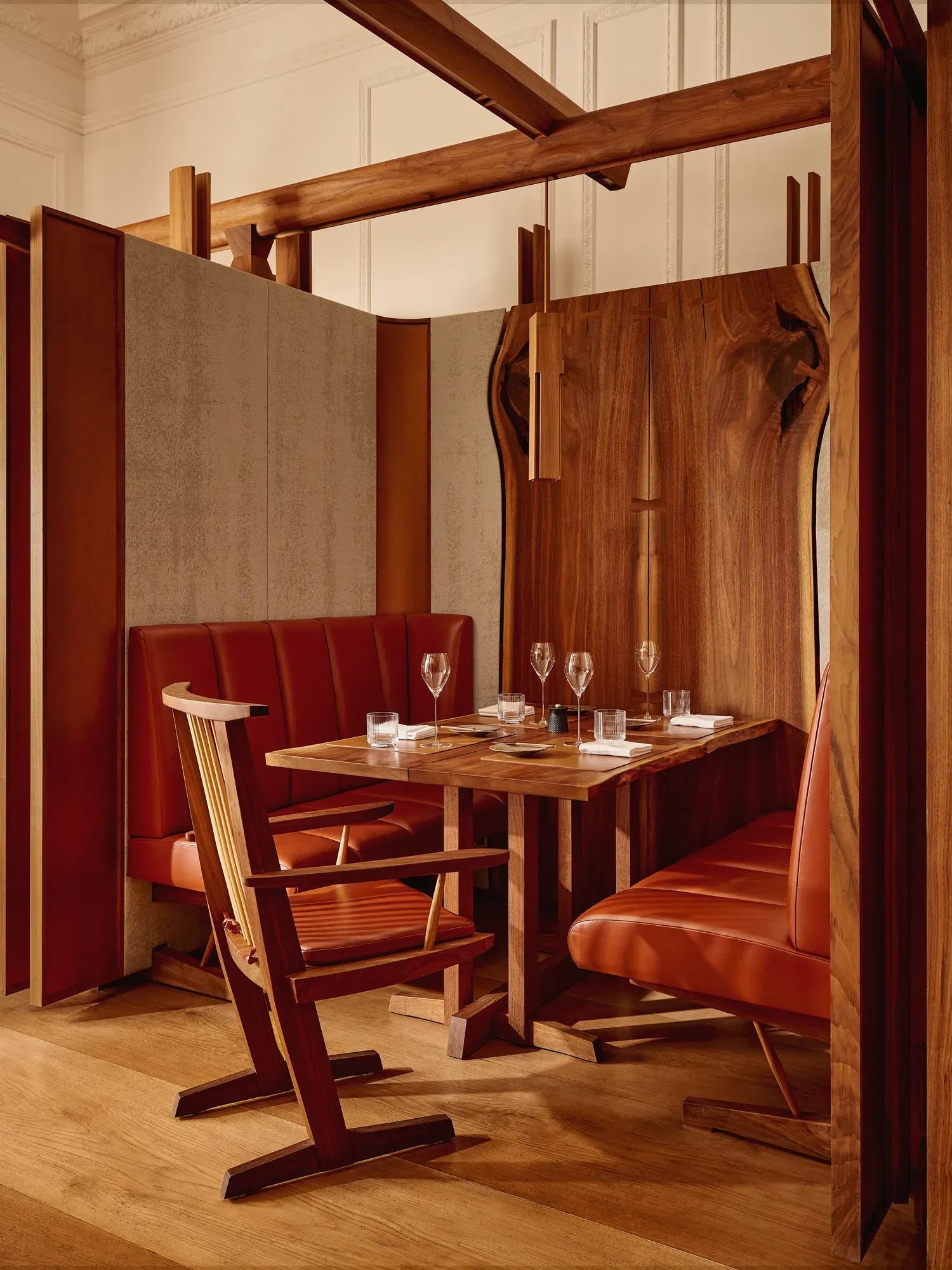 Wood-accented restaurant booth with red leather seating, a set table, and modern lighting.