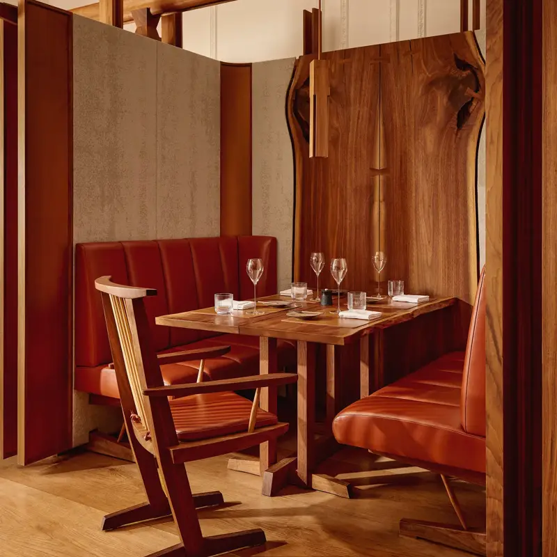 Wood-accented restaurant booth with red leather seating, a set table, and modern lighting.
