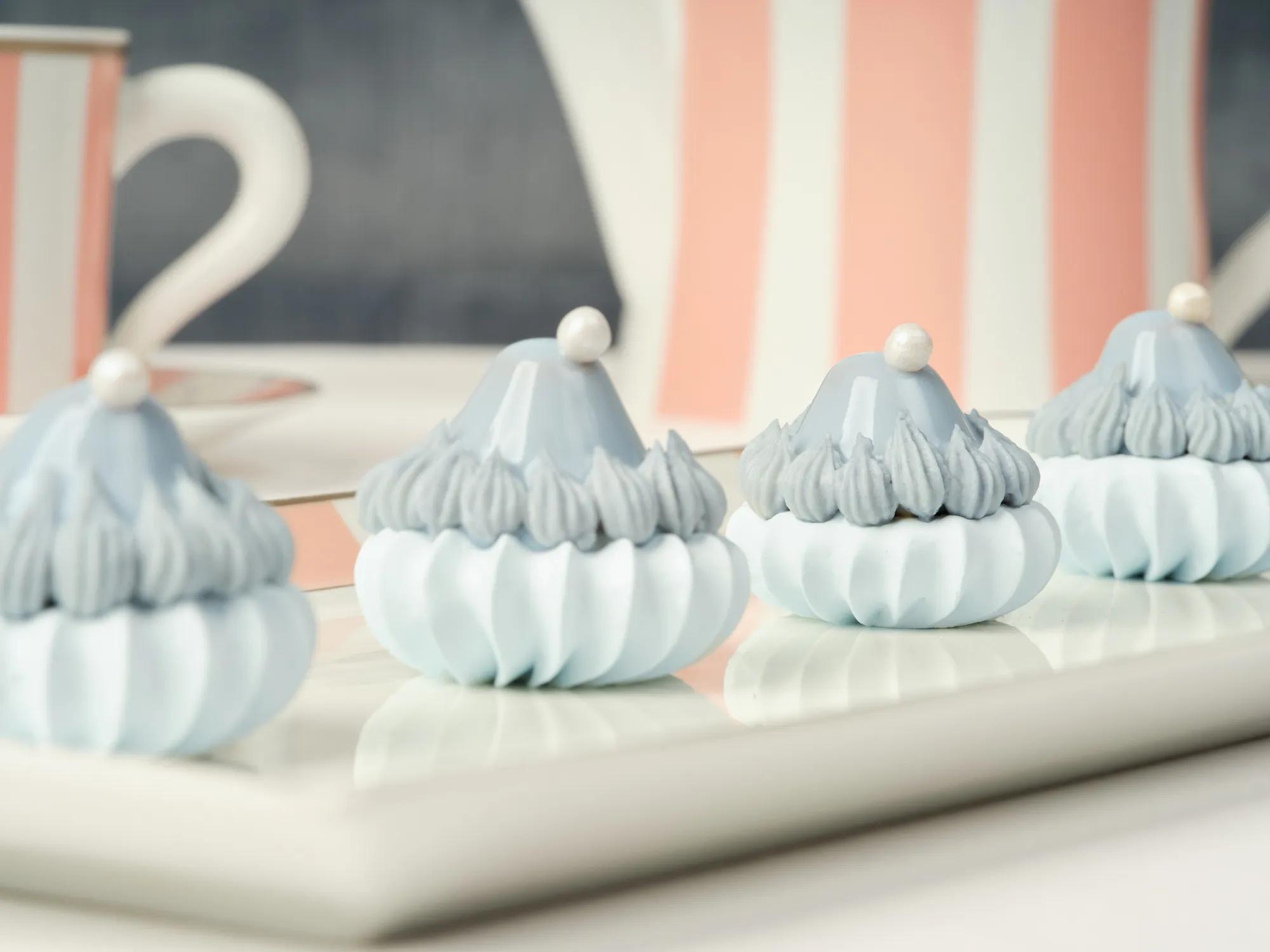 Close-up of blue-and-white meringue-style pastries with pearl toppers on a pink striped tray.