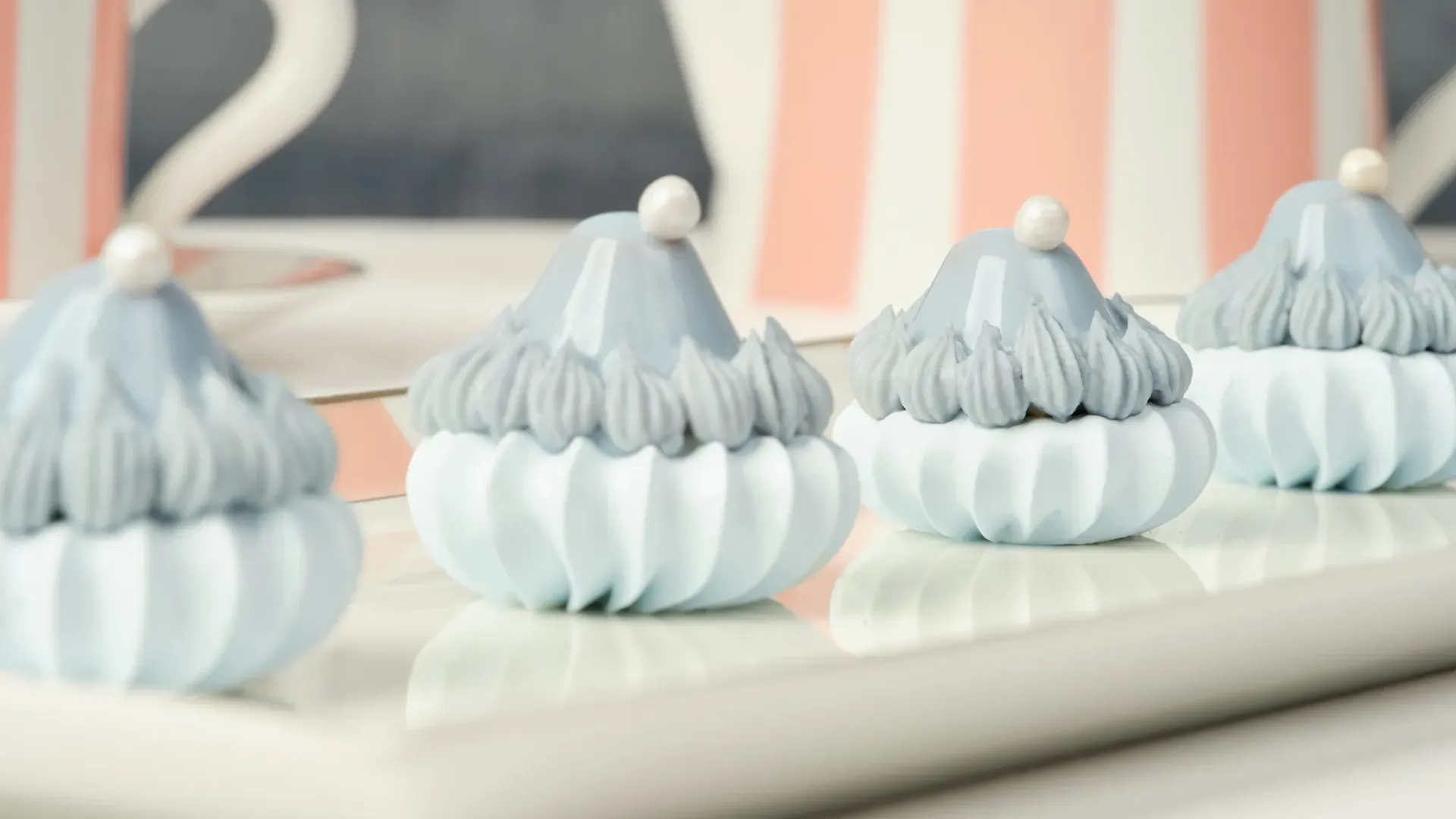 Close-up of blue-and-white meringue-style pastries with pearl toppers on a pink striped tray.