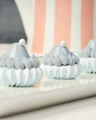 Close-up of blue-and-white meringue-style pastries with pearl toppers on a pink striped tray.