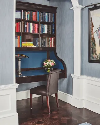Built-in writing nook with dark wood desk, bookshelves filled with colorful books, and a single chair.