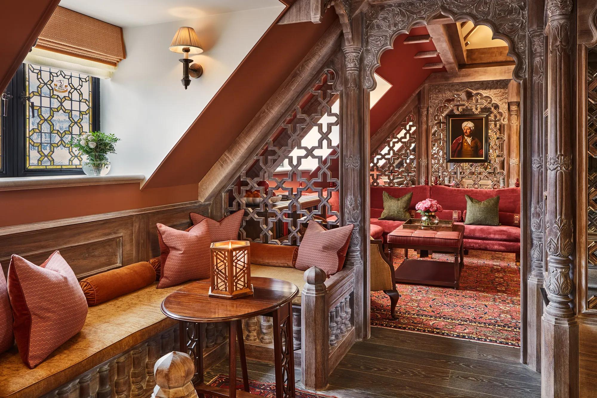 Cosy alcove seating with carved wood screens, red upholstery, patterned rug, and stained glass window in a richly detailed room.