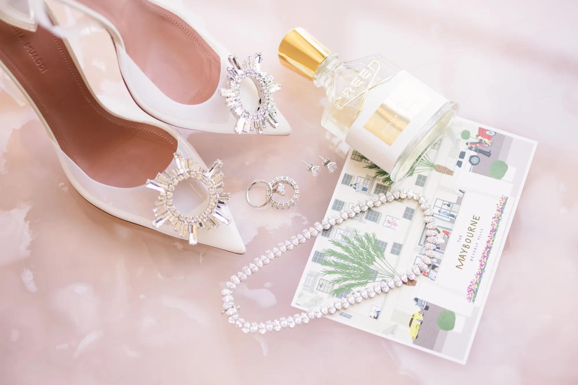 Flat lay of bridal accessories in Beverly Hills, including jeweled heels, diamond necklace, and Creed perfume.