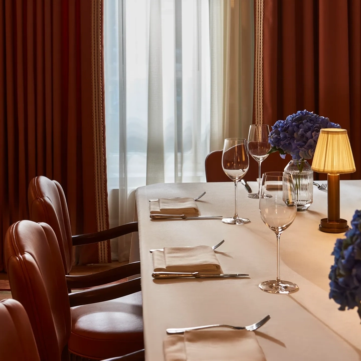 Private dining table set with red leather chairs, blue hydrangeas, and soft lamp lighting by window.