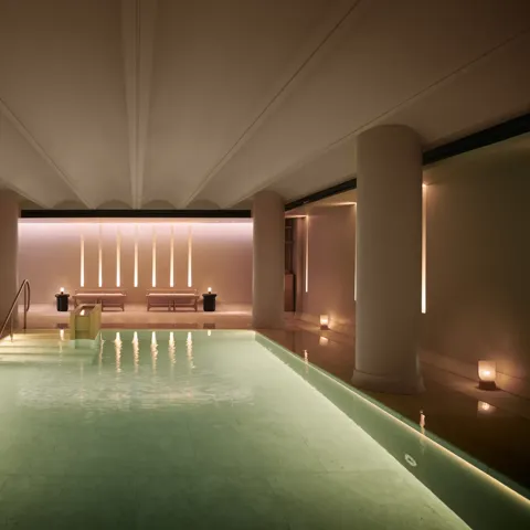 Serene indoor pool at Claridge’s spa, softly lit with candles and warm ambient lighting.