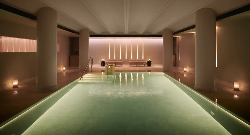 Serene indoor pool at Claridge’s spa, softly lit with candles and warm ambient lighting.