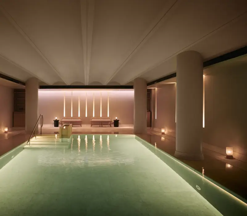Serene indoor pool at Claridge’s spa, softly lit with candles and warm ambient lighting.