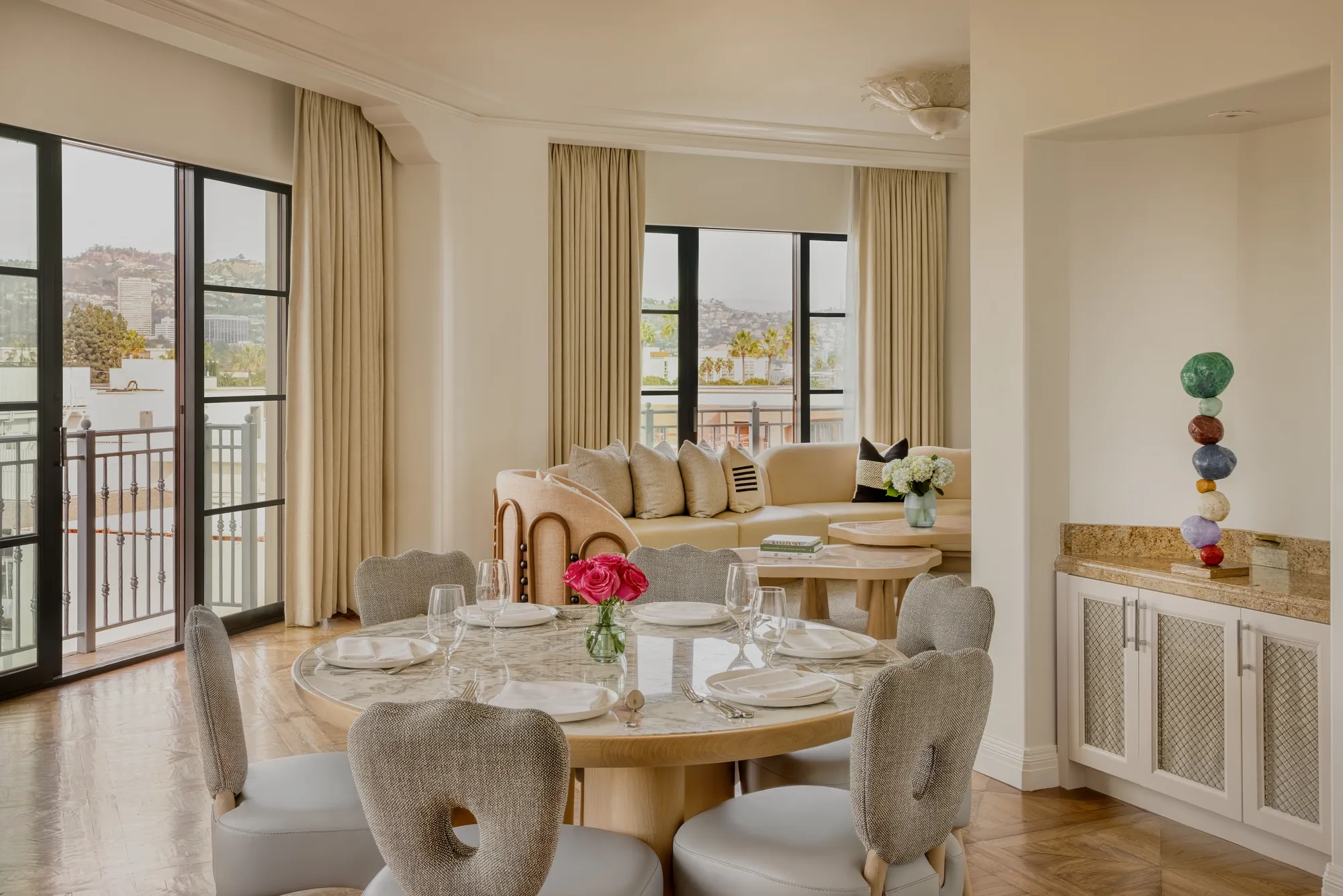 Hollywood Suite dining area with round table, cushioned chairs, with a curved couch in the foreground with Beverly Hills skyline views.