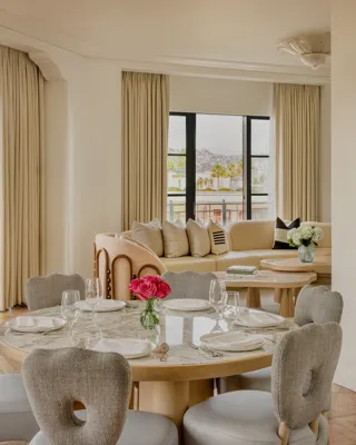 Hollywood Suite dining area with round table, cushioned chairs, with a curved couch in the foreground with Beverly Hills skyline views.