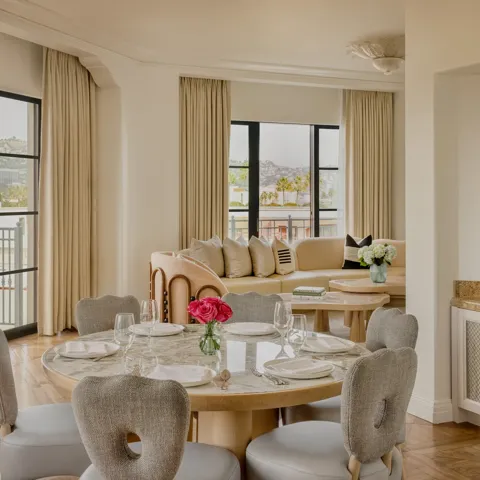 Hollywood Suite dining area with round table, cushioned chairs, with a curved couch in the foreground with Beverly Hills skyline views.